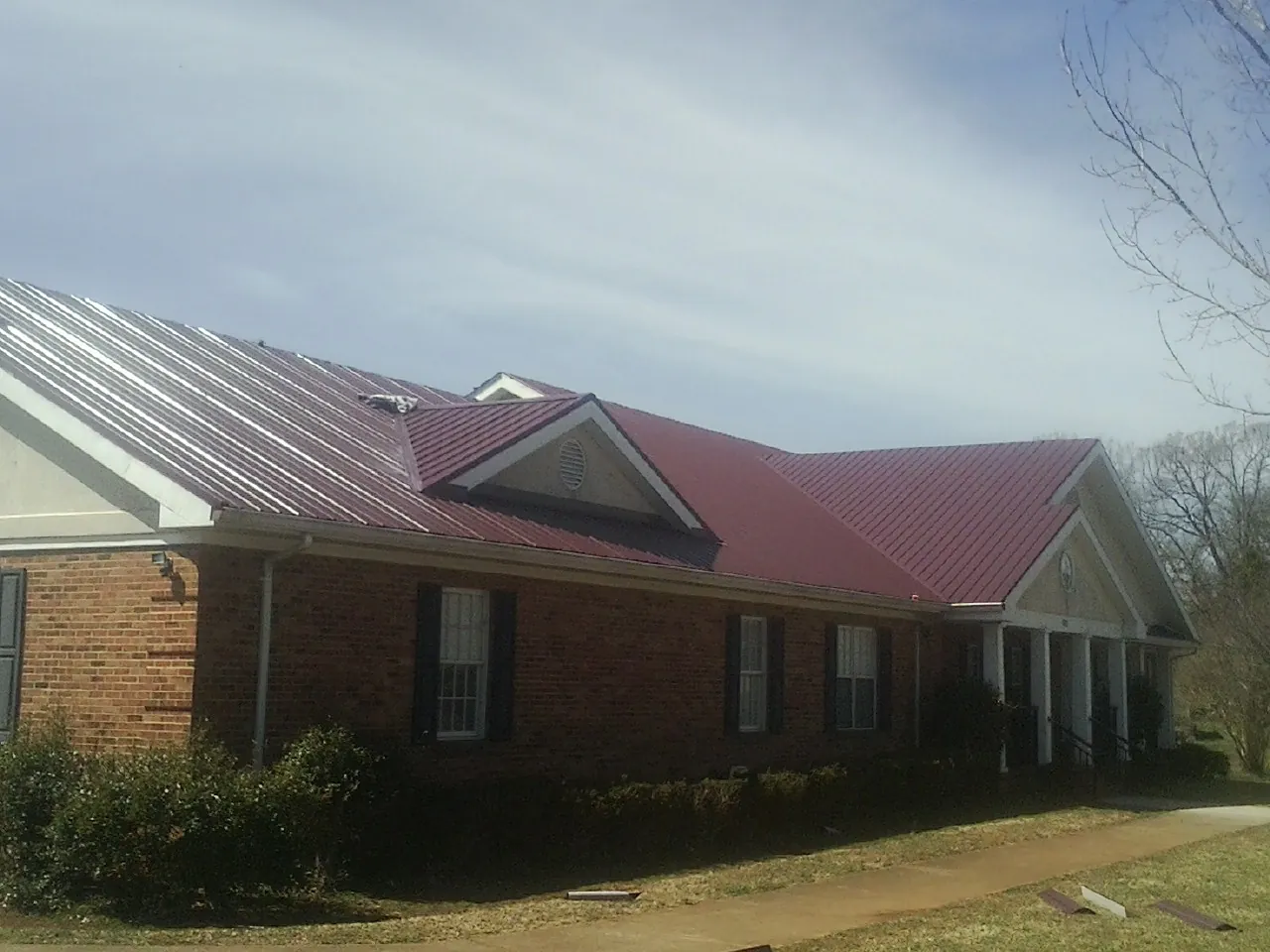 Red metal roof with gabled entries on a long brick building, from a Hail Damage Roof Repair job in Harrison Township