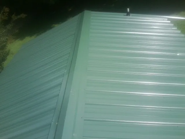 New green metal panels meeting at the ridge of a roof — Flat Roof Repair work by our crew in Harrison Township