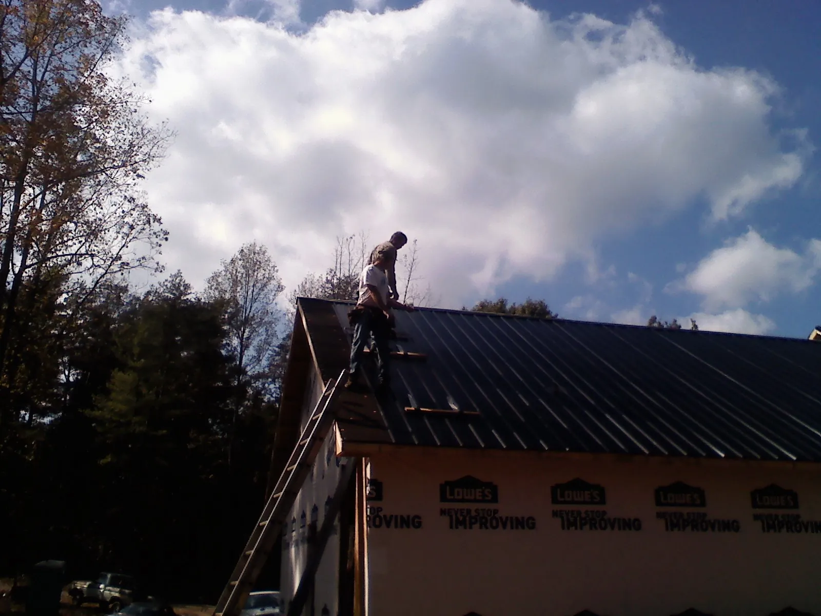 Roofer fastening dark metal panels high against a cloudy sky, from a Roof Inspection job in Harrison Township