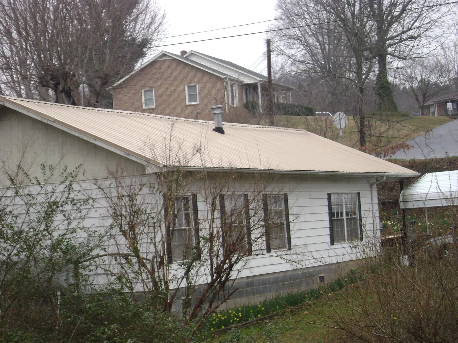 Tan metal roof on a white sided house set into a hillside — Commercial Roofing by Roofing Brothers in Harrison Township